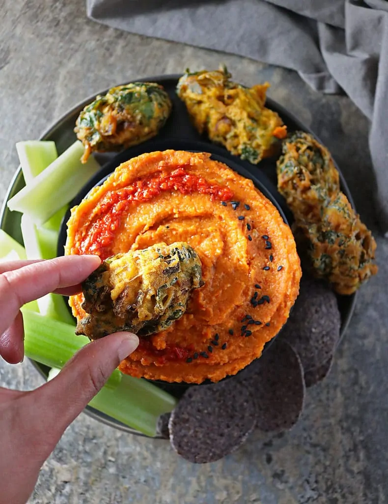 Overhead view of pakora being dipped into butternut squash dip with celery and chips on plate