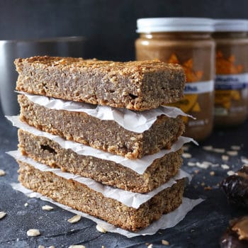 Stack of four Date Almond Bars with almond butter jars in the background.