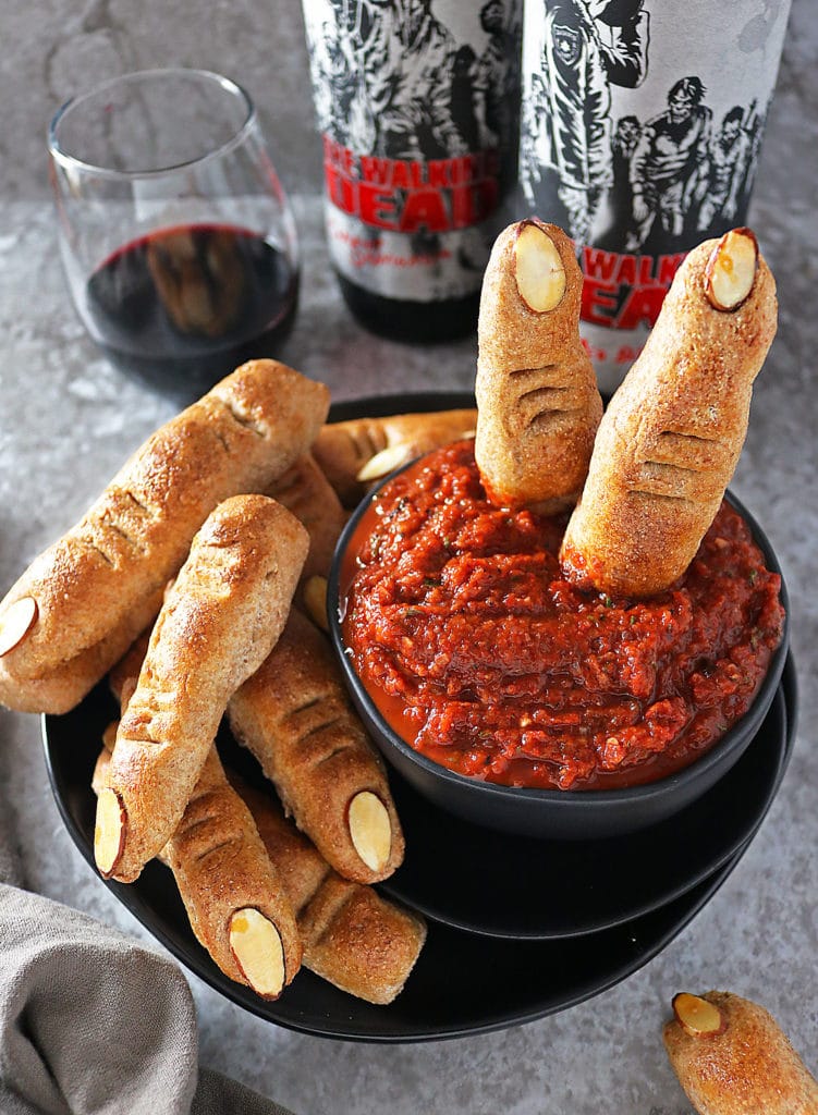 Finger Breadsticks placed in a plate and in a bowl with Red Pepper Red Wine Dip and wine bottles in the background