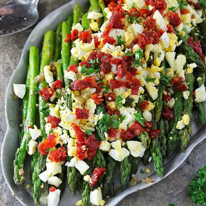 Sauteed Asparagus topped with boiled egg and sundried tomatoes on a silver platter