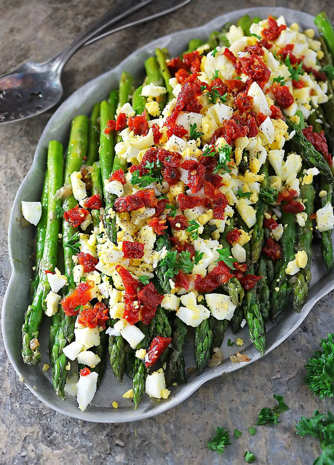 Sauteed Asparagus topped with boiled egg and sundried tomatoes on a silver platter