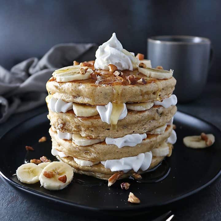Stack of Pecan Banana Pancakes with layers of bananas and whipped cream
