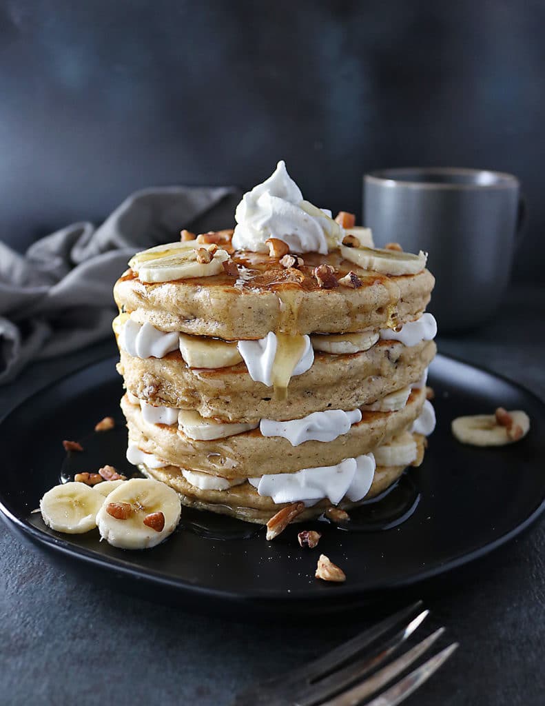 Stack of Pecan Banana Pancakes with layers of bananas and whipped cream