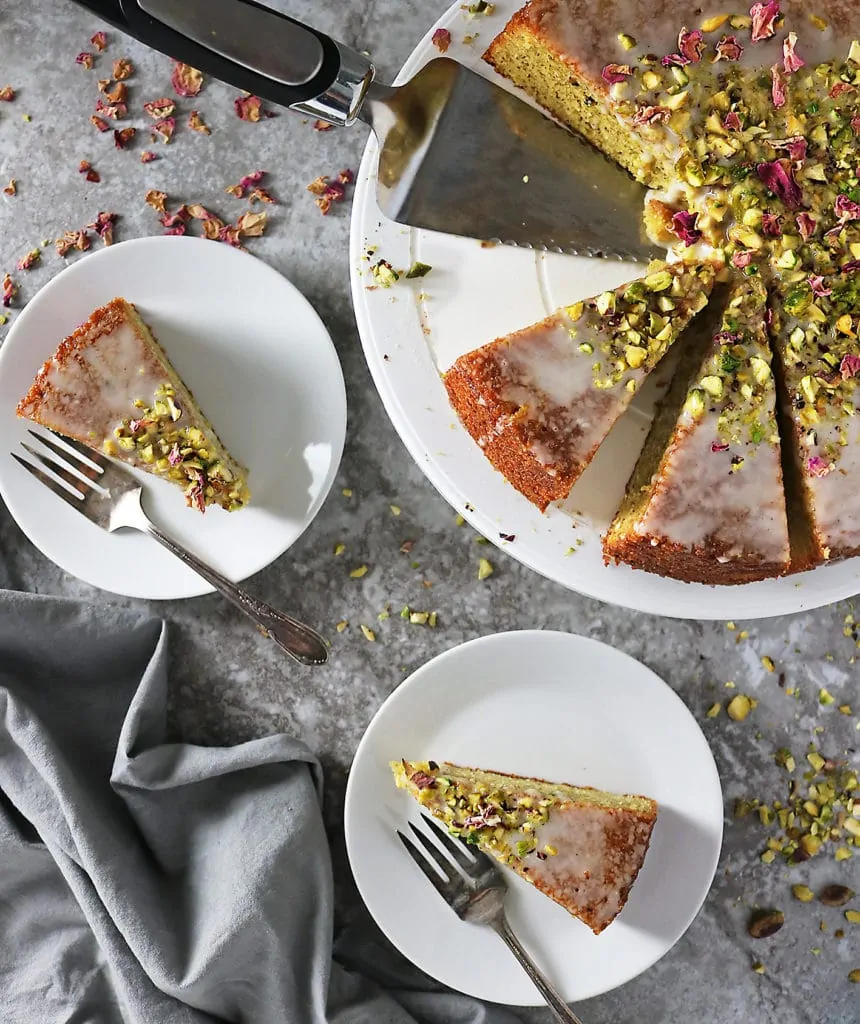 Overhead photo of Ottolenghi's Pistachio Rose Cake with two slices on dessert plates with forks