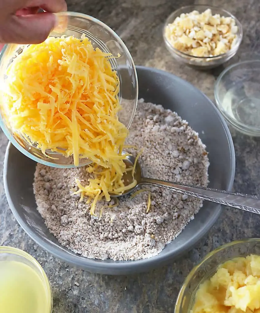 Photo of bowl with Shredded Tillamook Cheddar being emptied into another bowl with ingredients for making pineapple casserole
