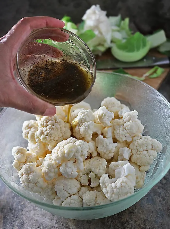 Cauliflower being tossed with olive oil, oregano and coriander
