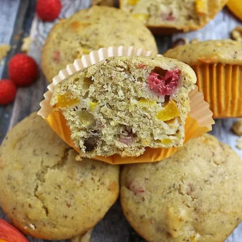 Photo of A Gluten Free Nutty Vegan Peach Raspberry Muffin cut in half with other whole ones
