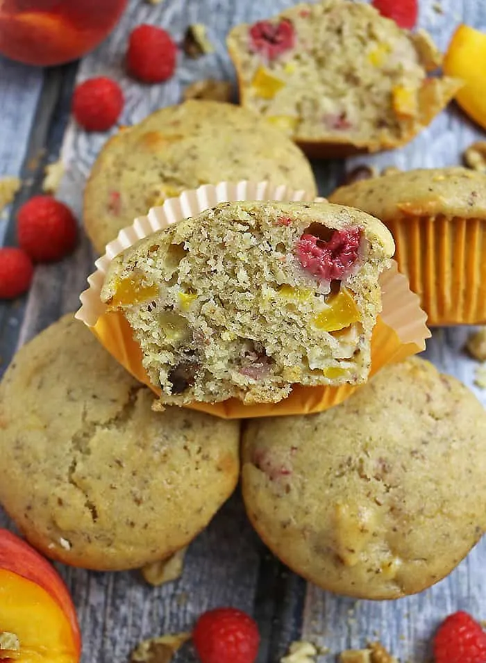 Photo of A Gluten Free Nutty Vegan Peach Raspberry Muffin cut in half with other whole ones