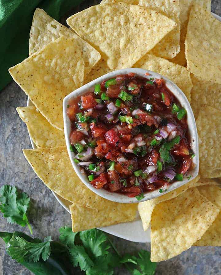 A bowl with easy homemade salsa with jalapeno surrounded with corn tortilla chips.