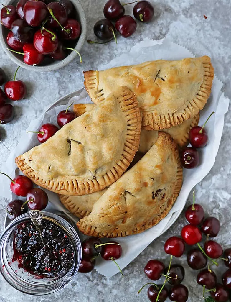 A plate of Savory cherry hand pies with chicken along with fresh cherries scattered around.
