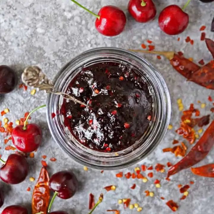 jar with delicious easy chili cherry sauce and cherries and whole chilies scattered around it.