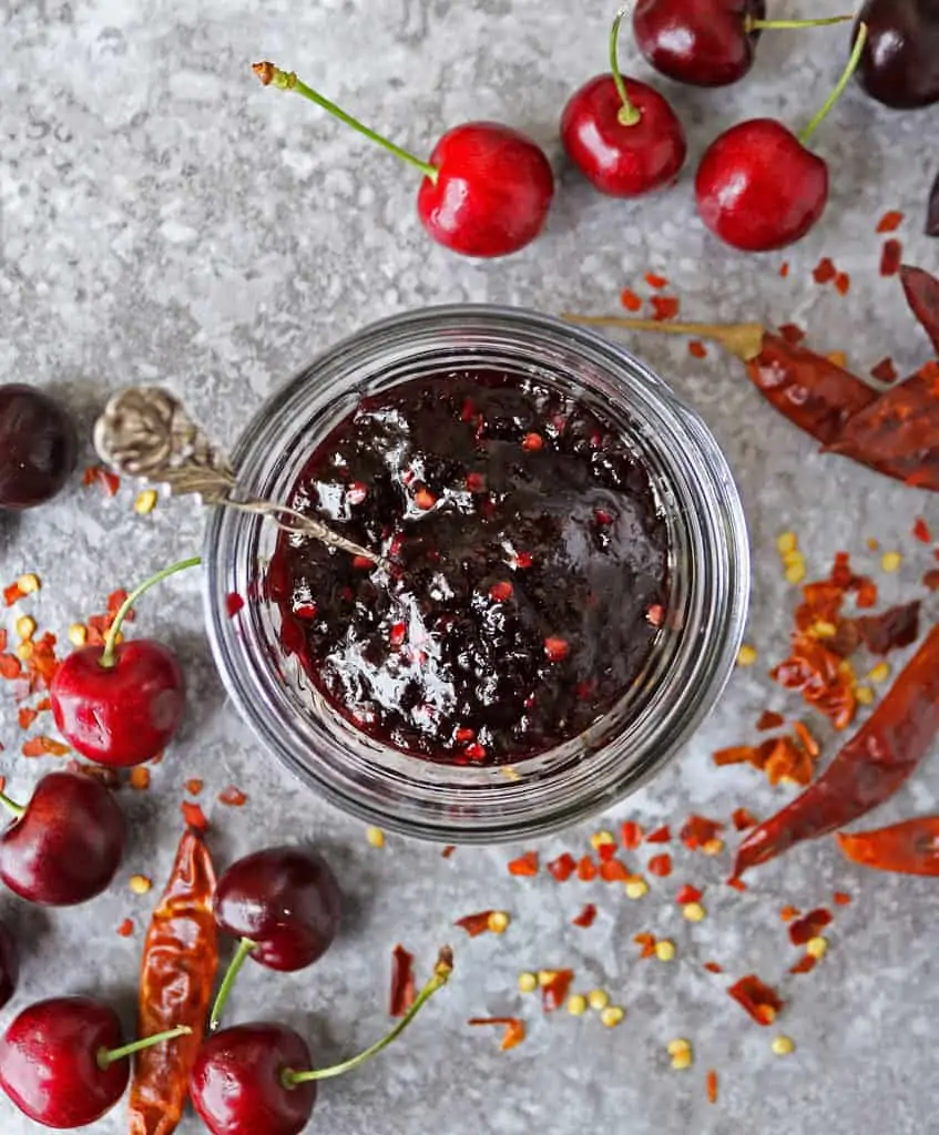 jar with delicious easy chili cherry sauce and cherries and whole chilies scattered around it.