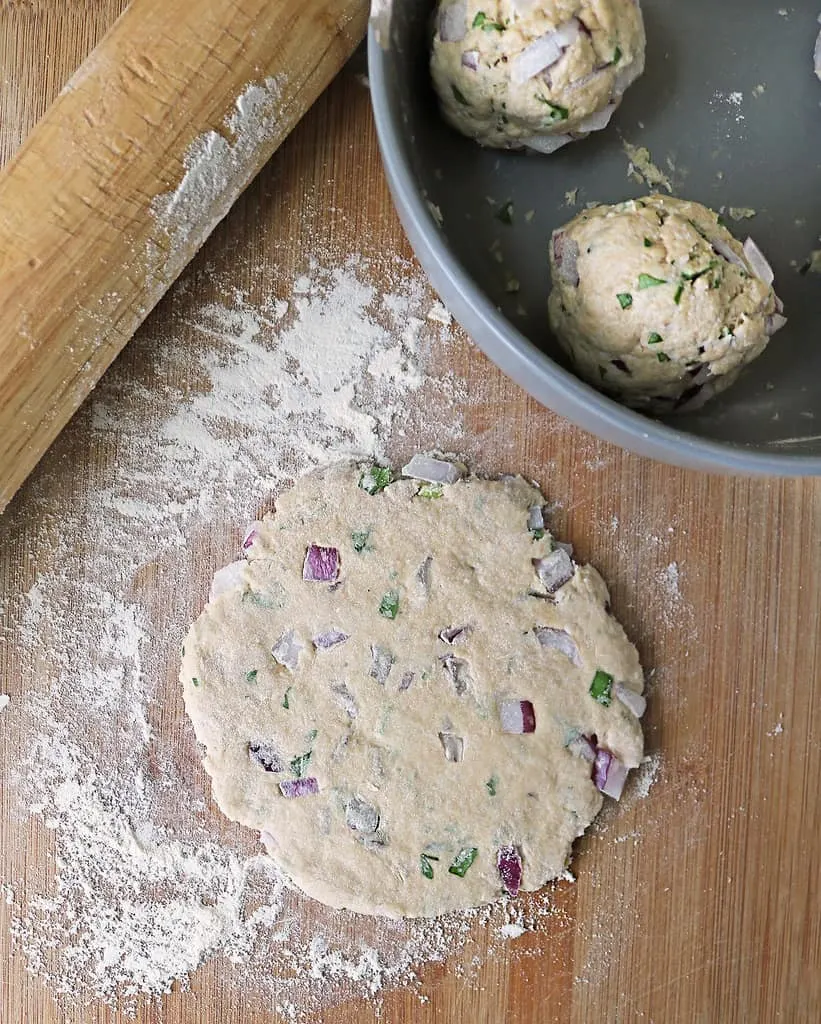 rolling out balls of pol roti with onion and herbs before cooking them on a hot stove.