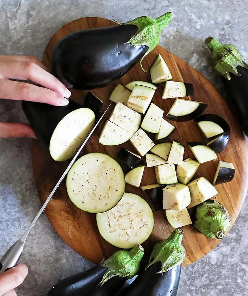 Chopping Eggplant into bite sized pieces on a cutting board.