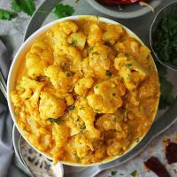 Easy Vegan Cauliflower Curry With Pumpkin in a bowl with condiments by its side.