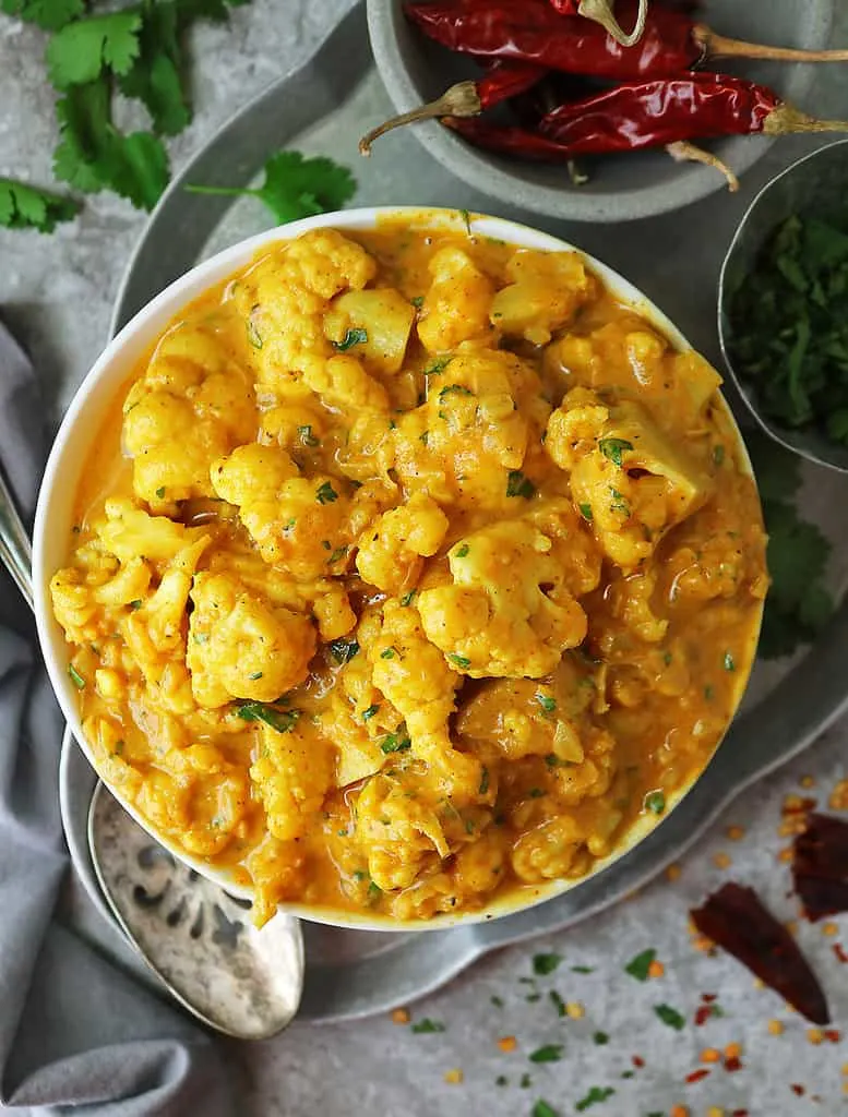 Easy Vegan Cauliflower Curry With Pumpkin in a bowl with condiments by its side.
