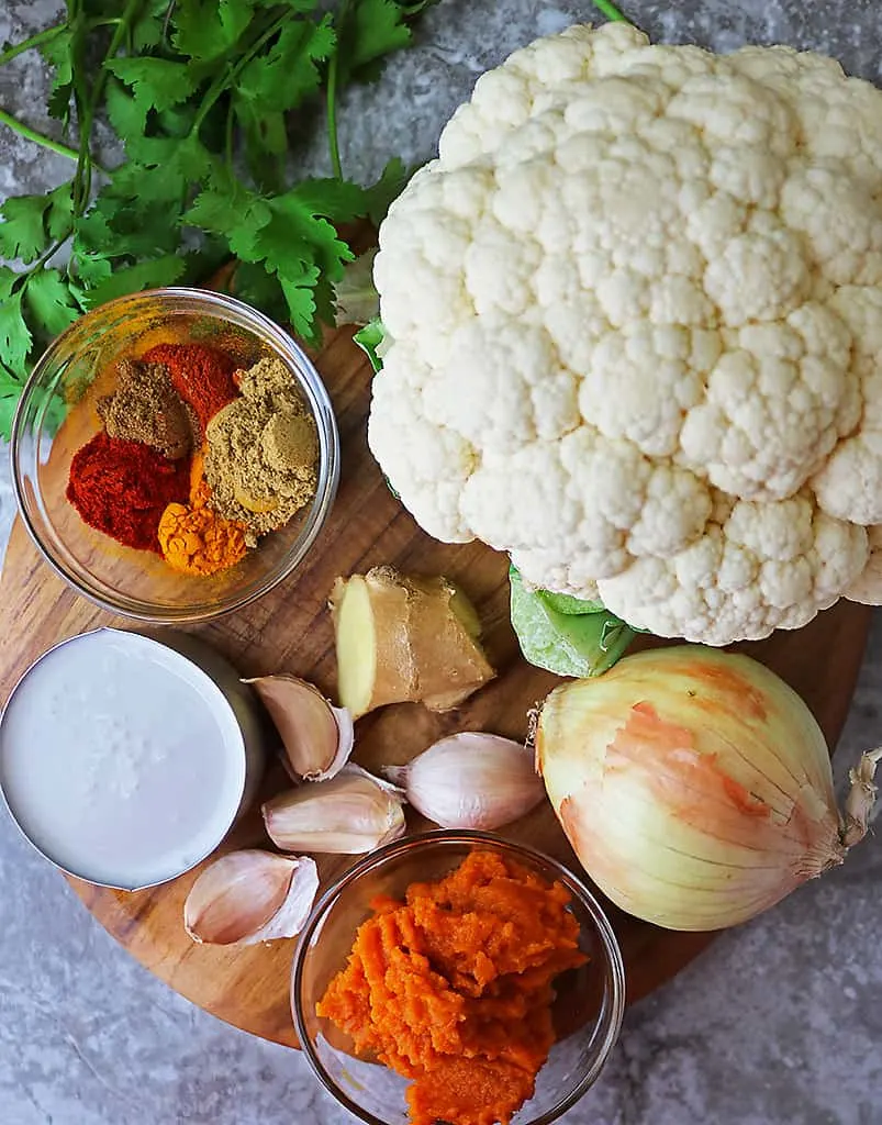 Ingredients to make cauliflower pumpkin curry on a cutting board.