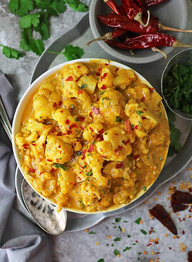 Vegetarian Pumpkin Cauliflower Curry in a bowl with small bowls of chili flakes and cilantro close by.