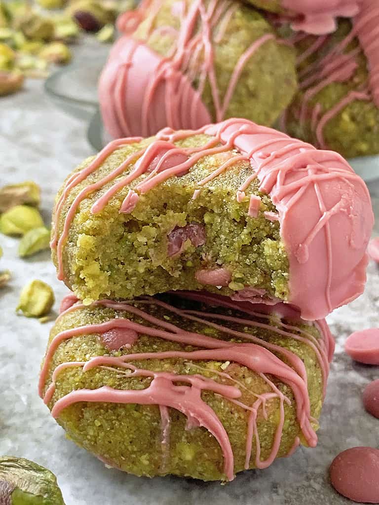 Two Gluten-free no-bake pistachio ruby chocolate cookies - one with a bite taken out of it.