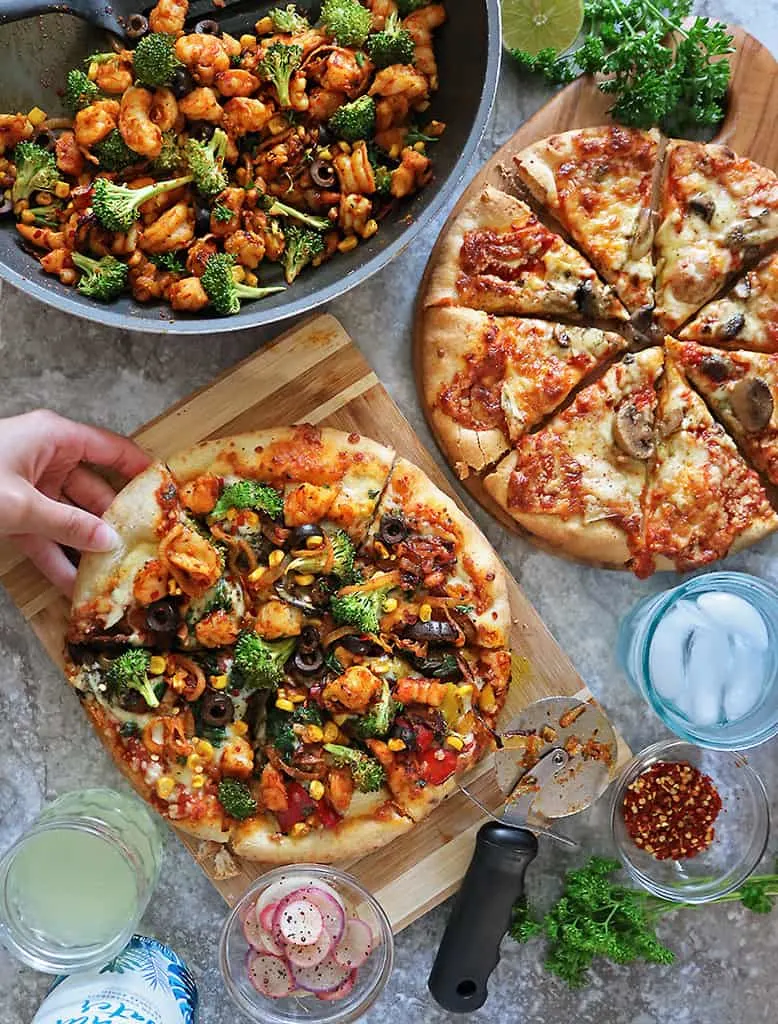 A loaded Frozen Pizza From Sprouts along with a mushroom pizza and a skillet with shrimp and broccoli saute.