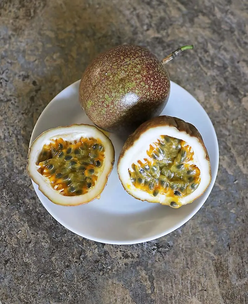 Tasty passion fruit cut in half on a plate next to a whole passion fruit.