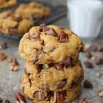 stack of 3 pumpkin chocolate chip cookies dairy-free with a glass of milk in the background.