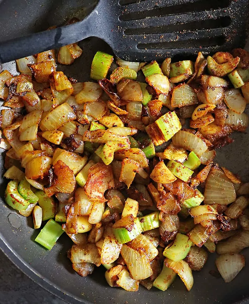 Adding spices and celery to onions ginger garlic saute to make spinach curry sauce