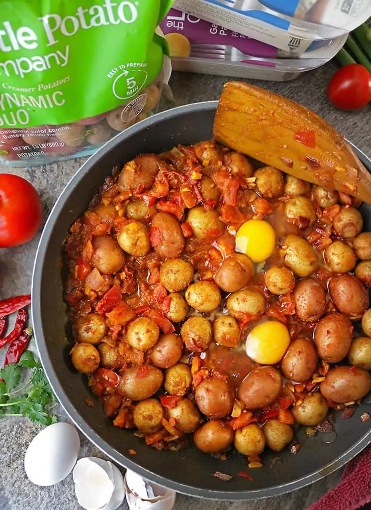 Making potato shakshuka by adding eggs to pan with potatoes and spices