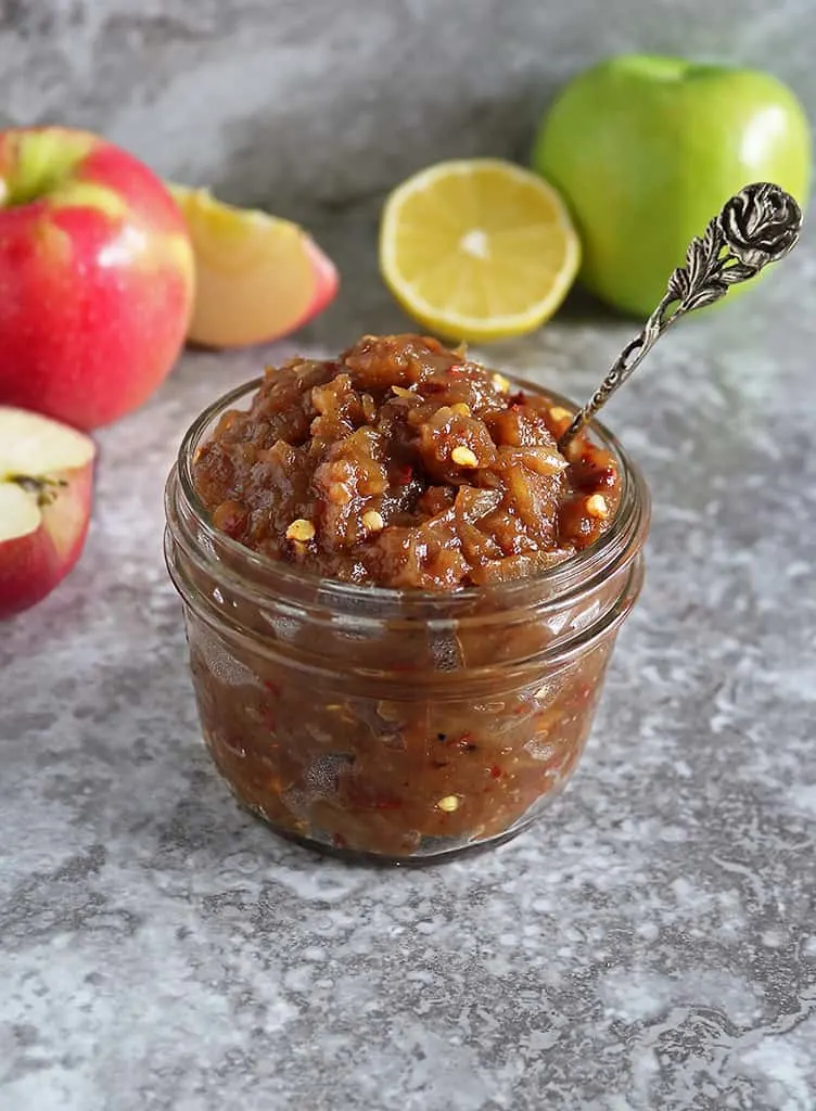 easy apple chutney in a glass container with apples in the background.