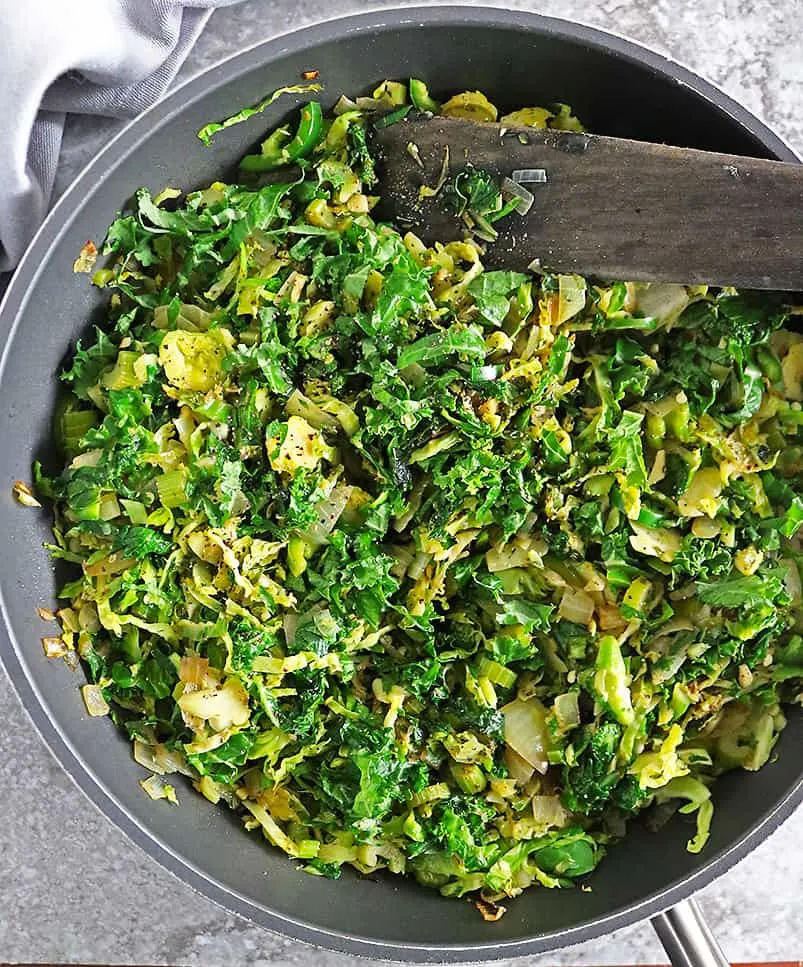 making Christmas Salad by adding kale to sauteed mix of brussels sprouts onions ginger garlic celery