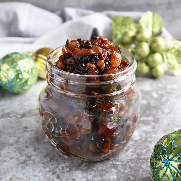 A homemade vegetarian mincemeat recipe in a glass jar with christmas decoration in the background.