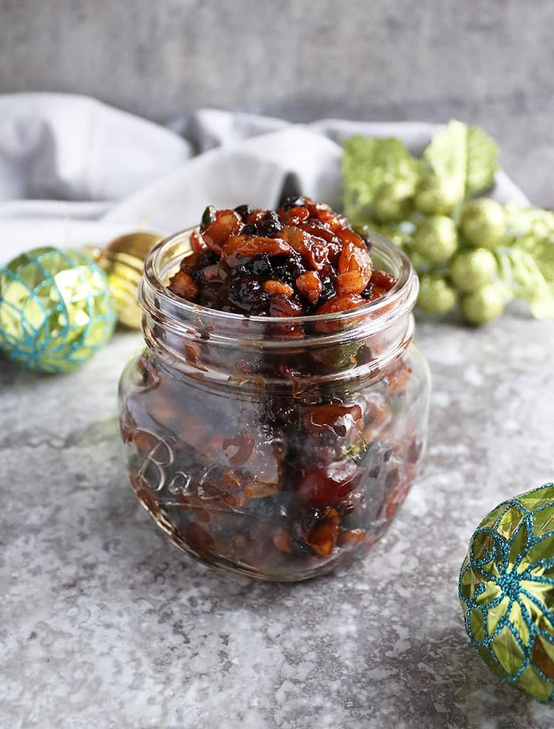 A homemade vegetarian mincemeat recipe in a glass jar with christmas decoration in the background.