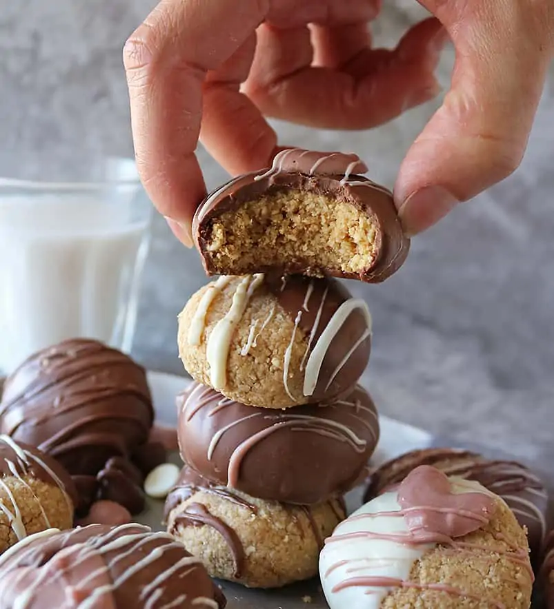 hand putting back an Eggless Almond Flour Peanut Butter Cookie dipped in chocolate after taking a bite out of it.