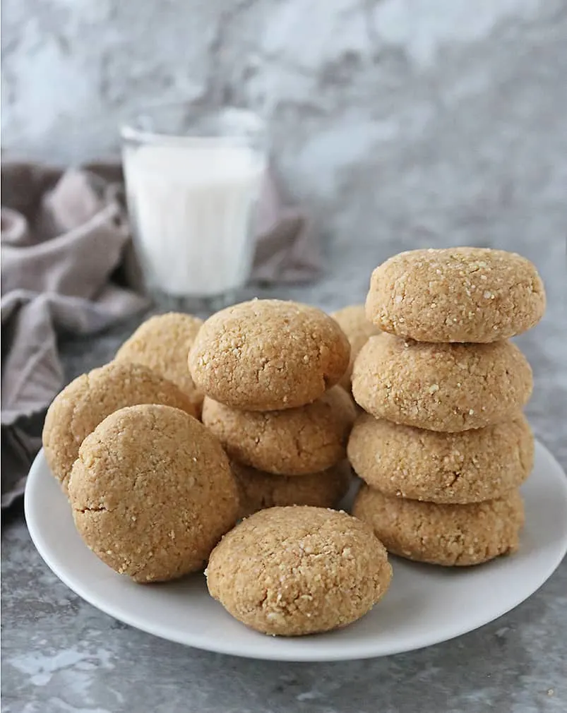 A batch of Tasty Eggless Almond Flour Peanut Butter Cookies with a glass of milk in the background.