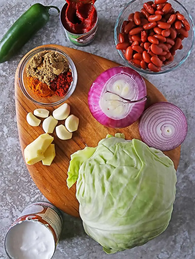 11 Ingredients to make cabbage bean soup laid out on a wooden platter.