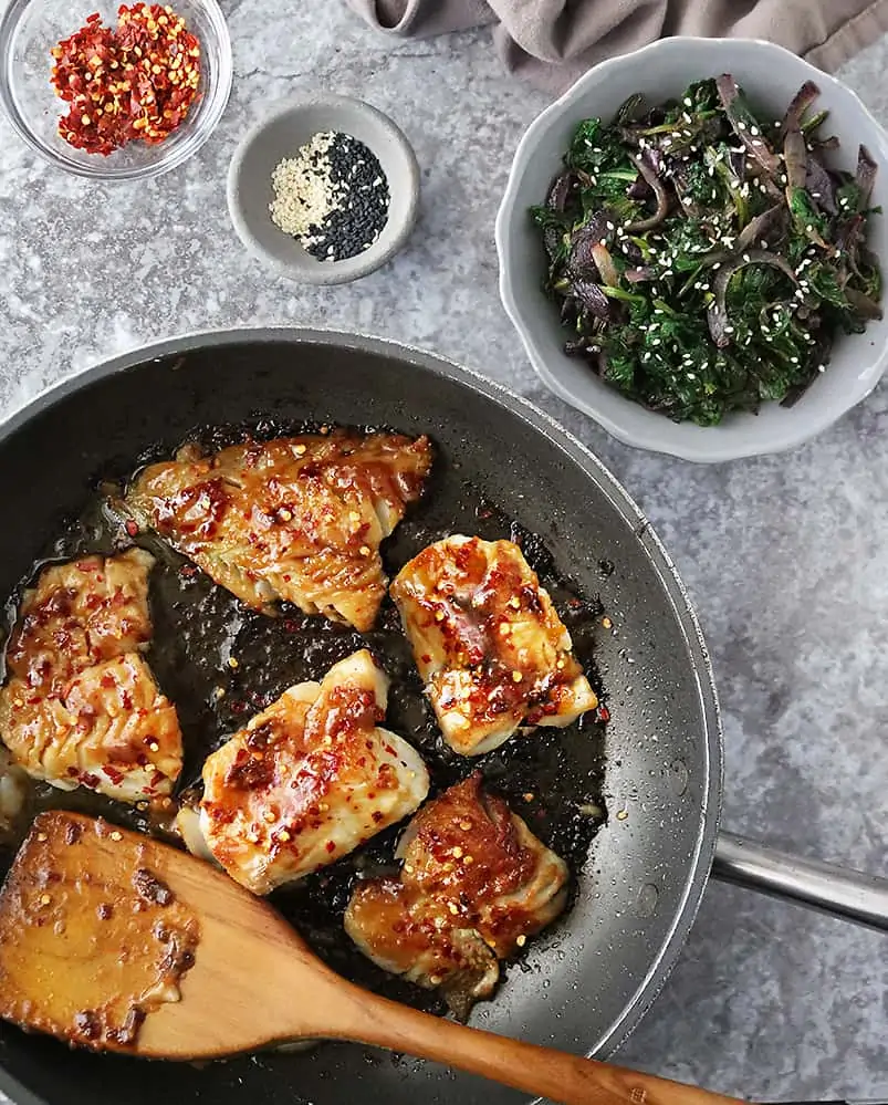 table set with pan with Cod and a bowl with Sauteed Soy Spinach & Onions.