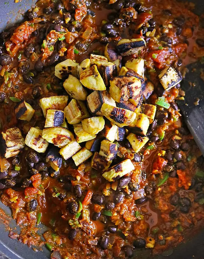 adding roasted plantains to vegan bean stew in a pan