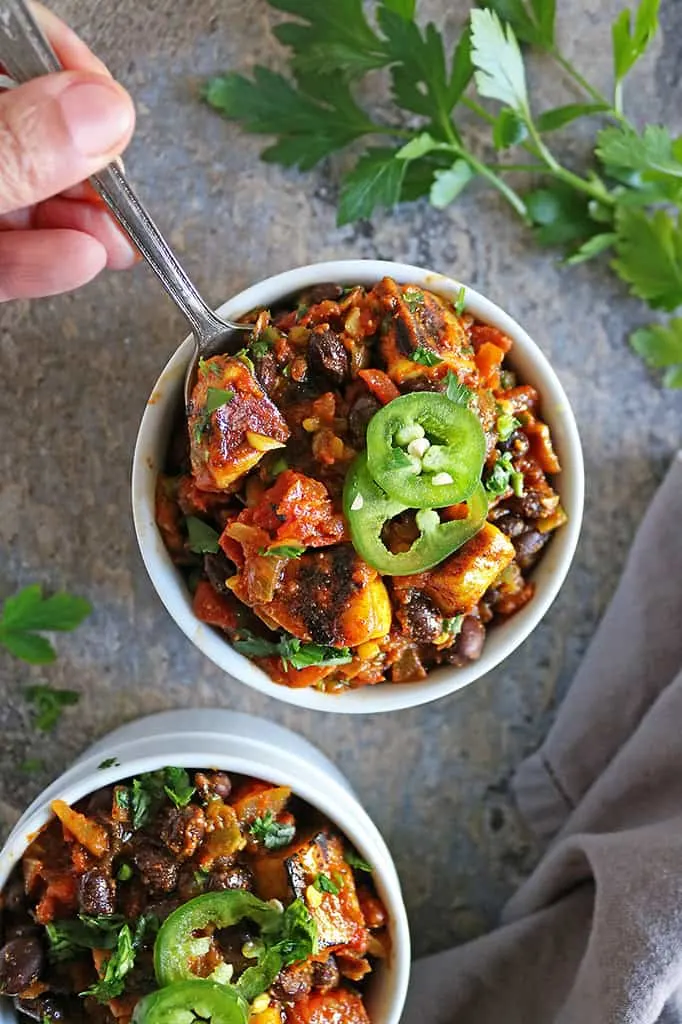 taking a spoon of vegan beans and plantain stew with roasted plantains