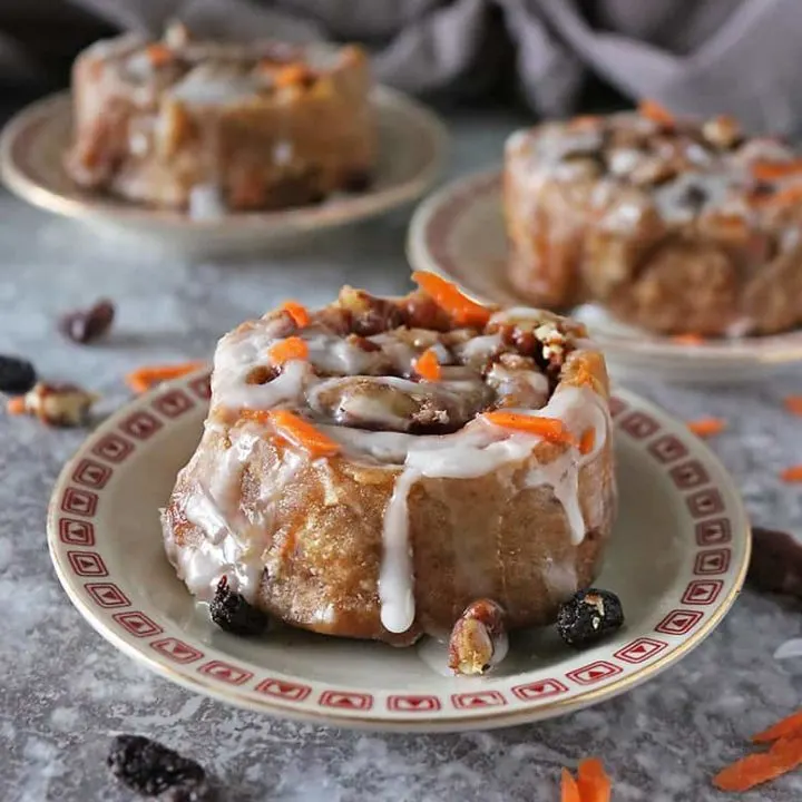 One carrot cake cinnamon roll on a plate with two others in the background