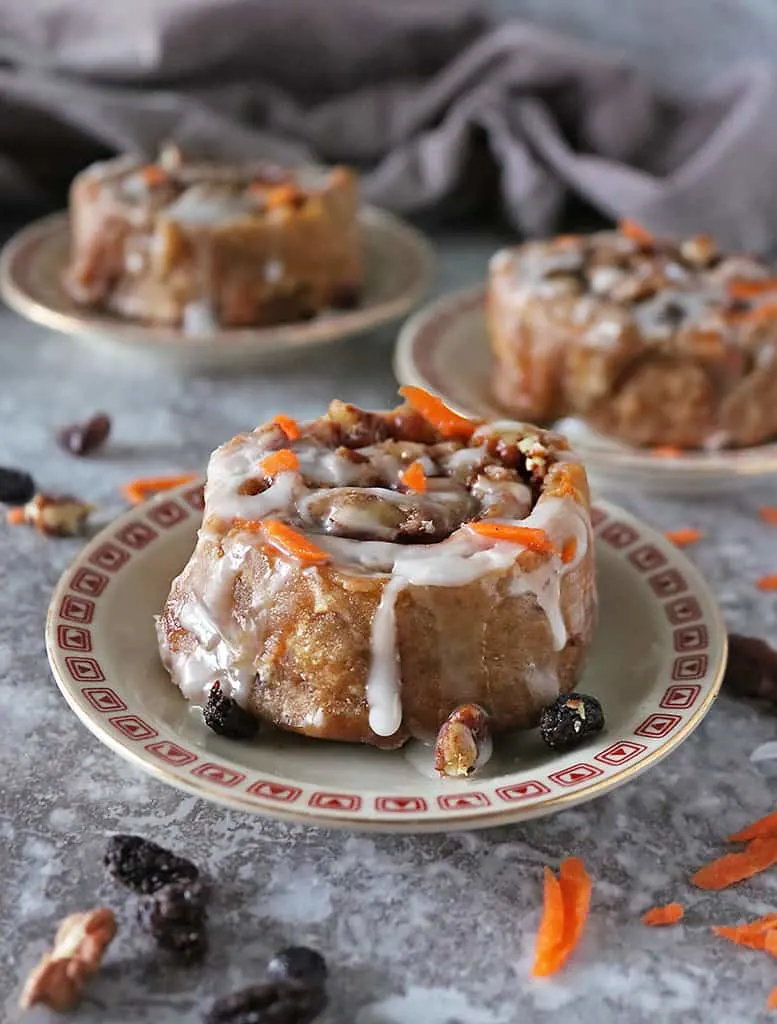 One carrot cake cinnamon roll on a plate with two others in the background