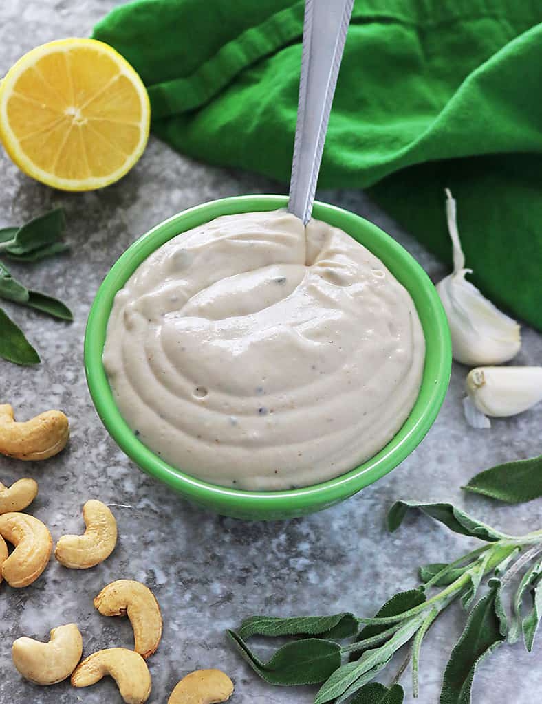 Plant-Based Creamy Garlic Sage Sauce in a bowl with cashews, lemons, sage around it.