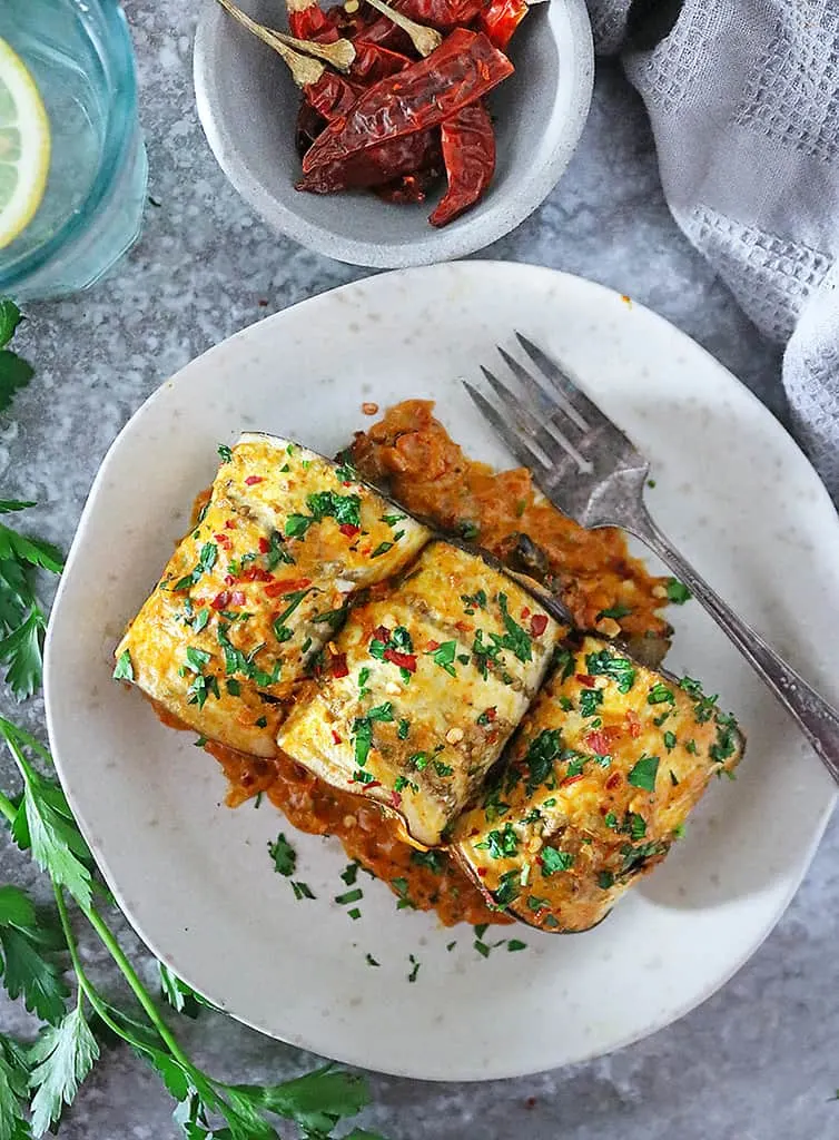 Three plant-based potato and bean stuffed eggplant rollatini on a plate.