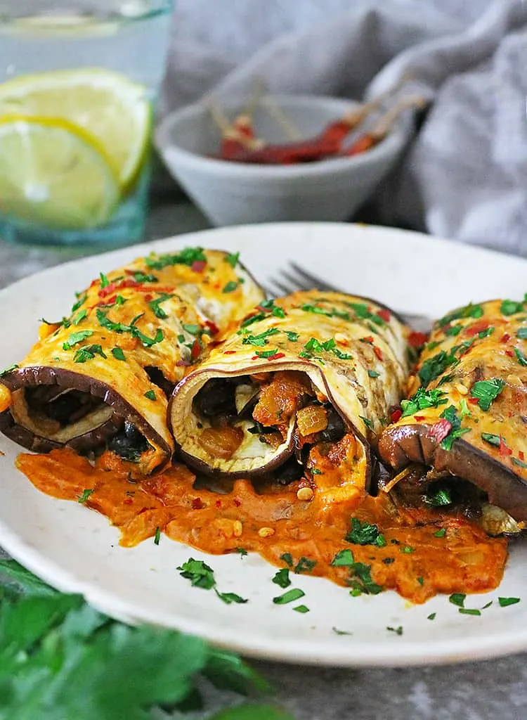 3 vegan eggplant rollatini on a plate with tomato coconut sauce.