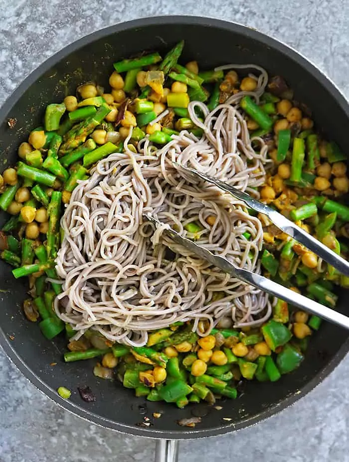Adding noodles to curry veggies for dinner in a large pan.