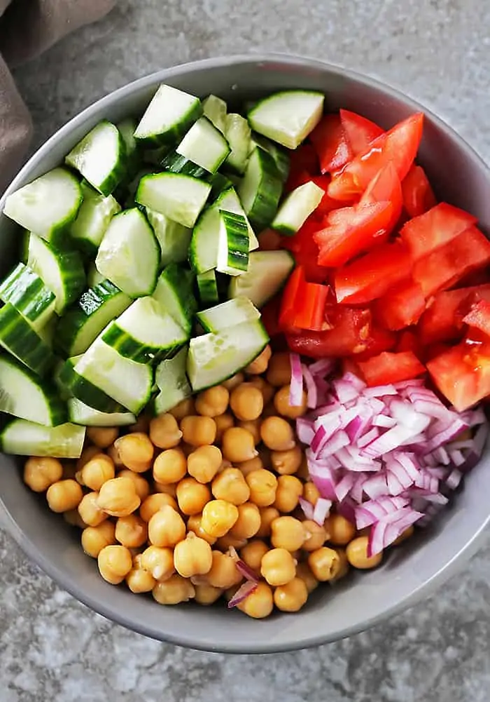 Prepping veggies to make vegan chickpea salad in a large grey bowl
