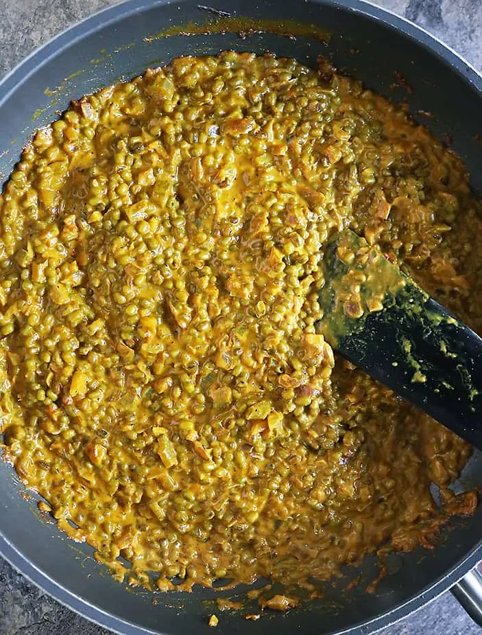 Stirring a simmering mung bean curry in a large pan on a stove top.