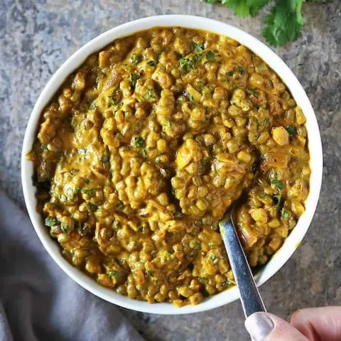 Taking a spoonful of this curry from a large serving bowl.
