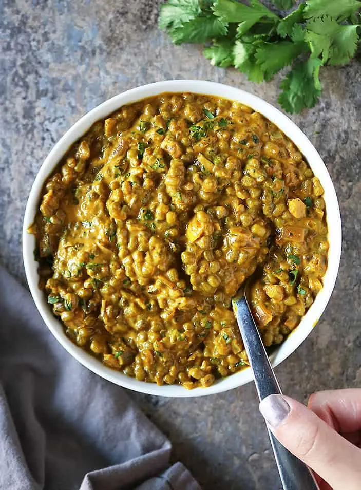 Taking a spoonful of this curry from a large serving bowl.