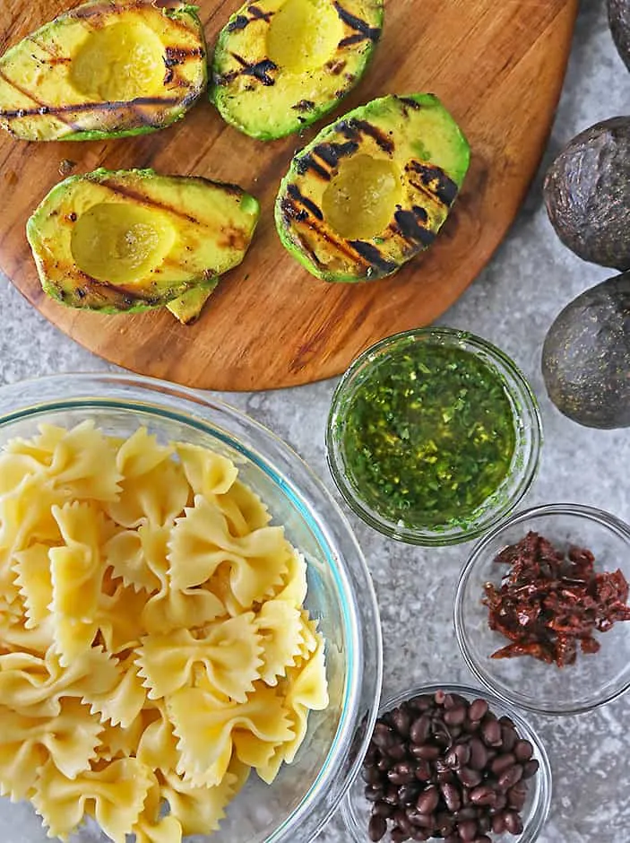 Overhead photo of grilled avocados, lemon dressing, cooked pasta, and sundried tomatoes.