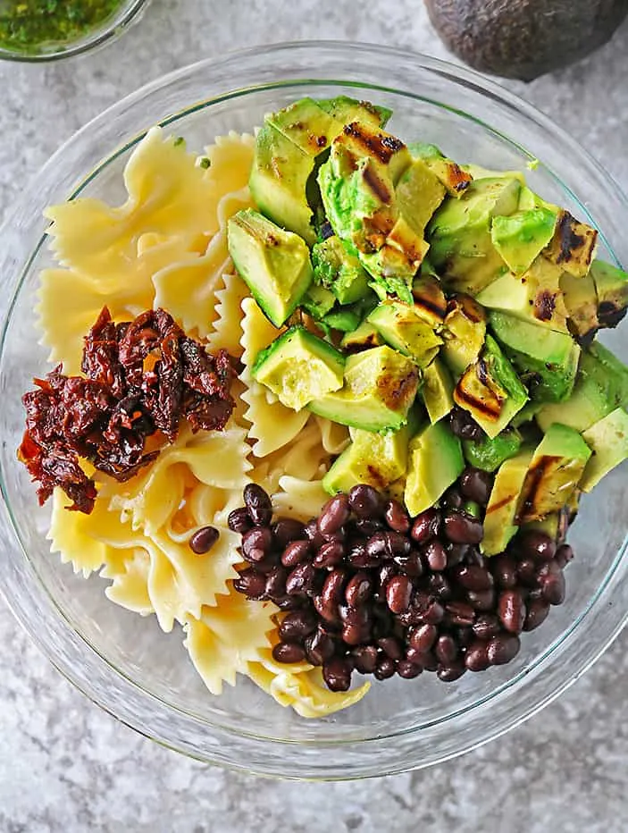 Overhead photo of a glass bowl with all the ingredients to make a healthy flavorful version of pasta salad.